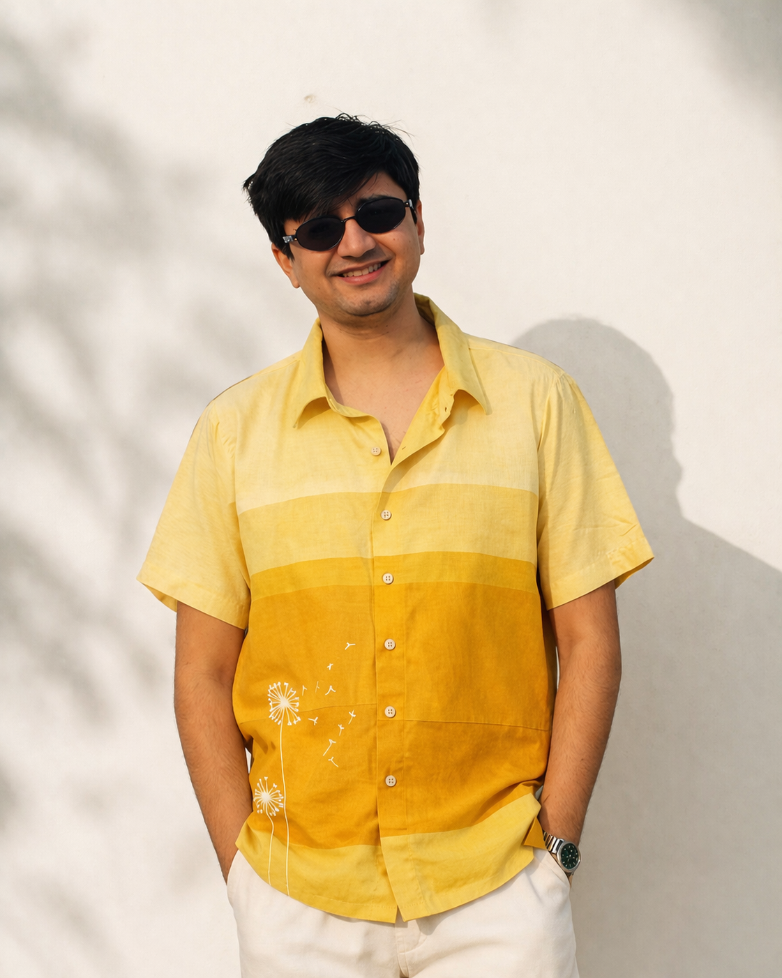Man wearing JOD's Dandelion Shirt - a yellow ombre patchwork cotton shirt with hand-painted dandelion detailing, styled with white trousers