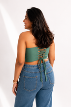 Woman wearing a green strapless top with lace-up back and blue jeans on a white background