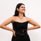 Woman wearing a black strapless dress with gold accents against a white background