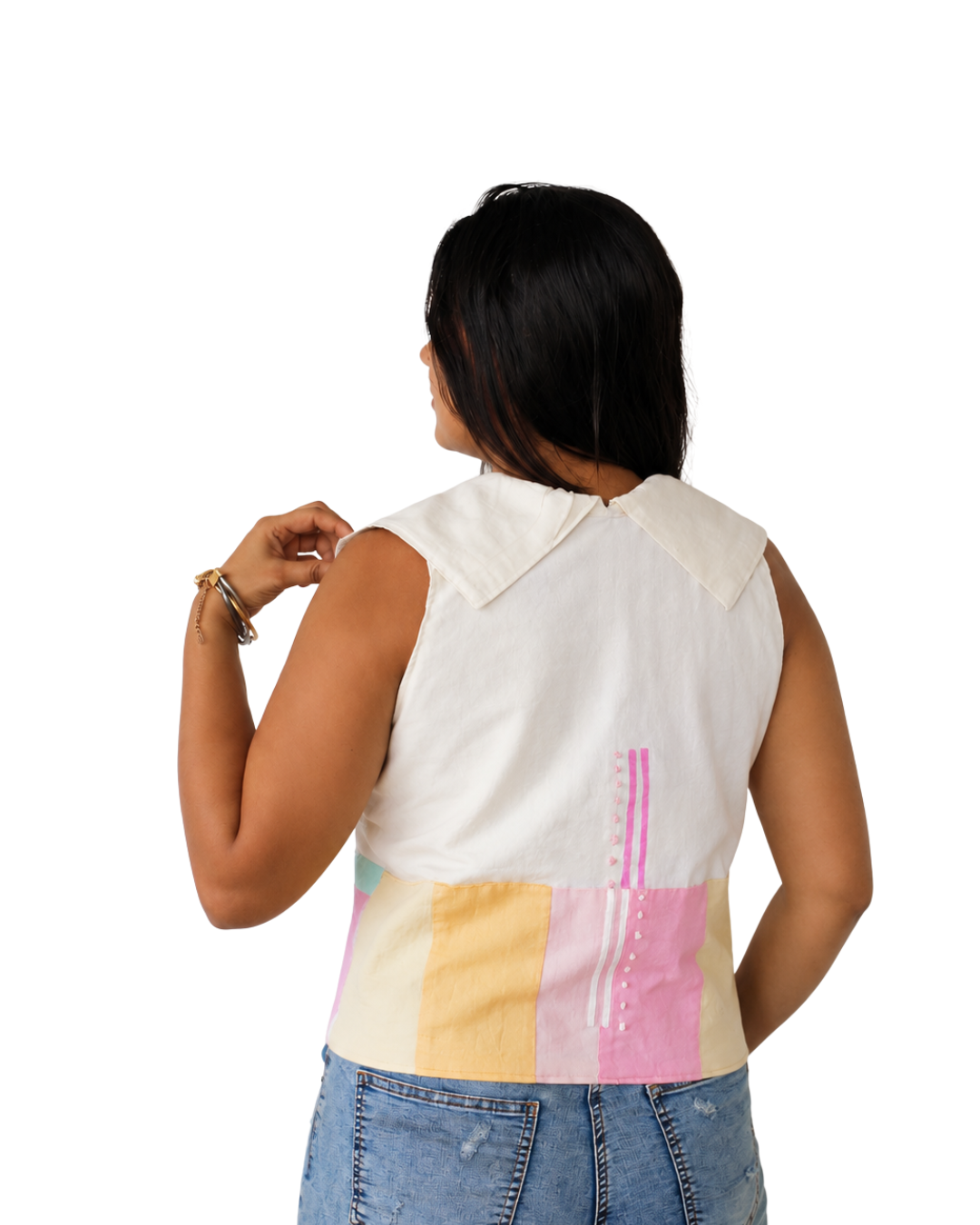 A woman shown from the back wearing a sleeveless collared top with a multicolor patchwork design in cream, yellow, and pink, paired with blue jeans against a white background.