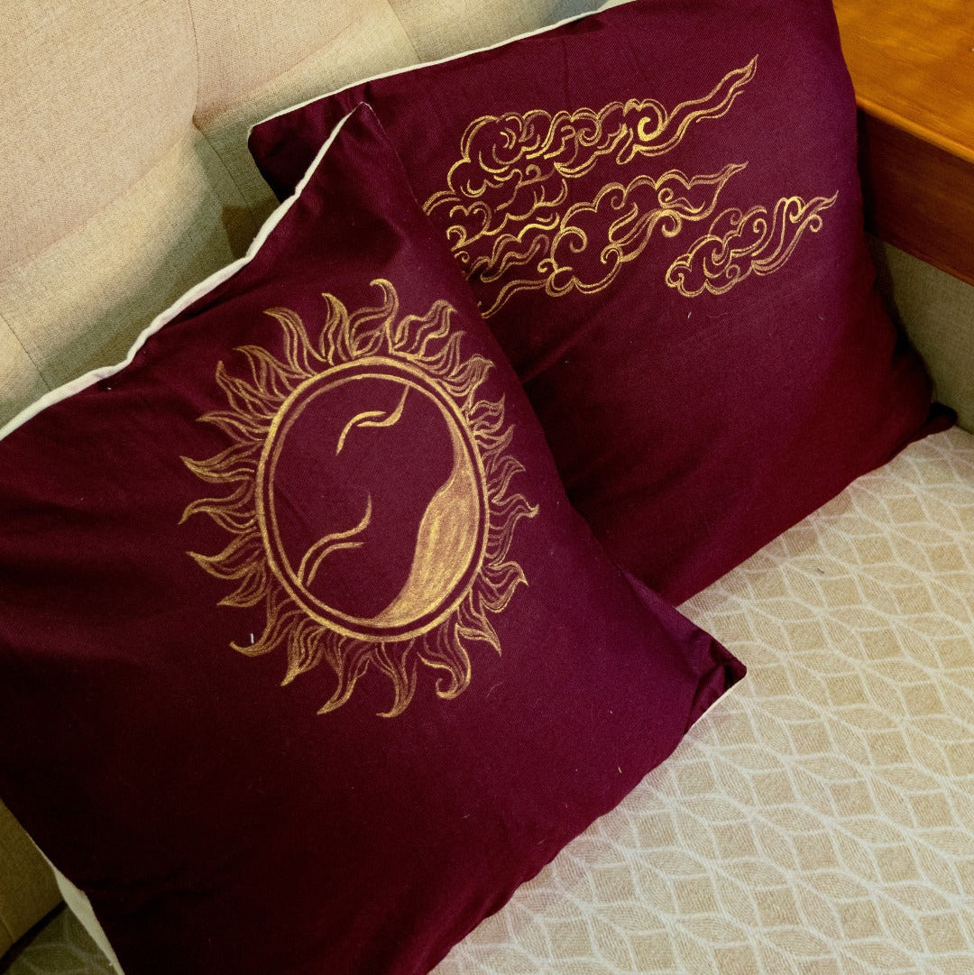 Maroon pillows with gold painted details on a beige couch.
