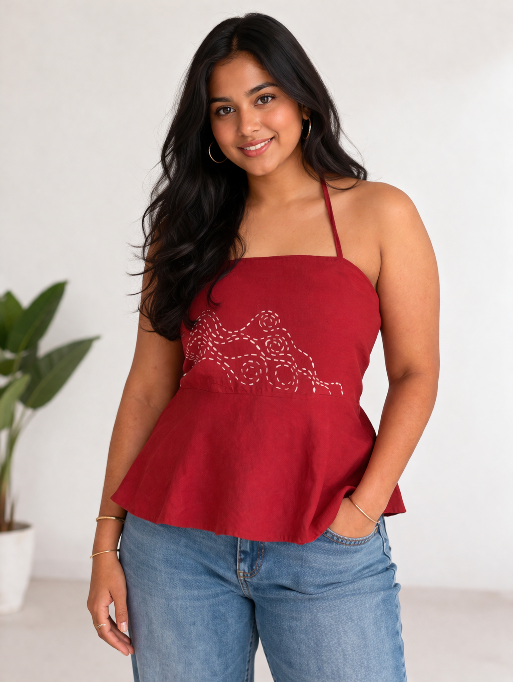 Woman wearing a red peplum halter top with floral embroidery and blue jeans against a white background