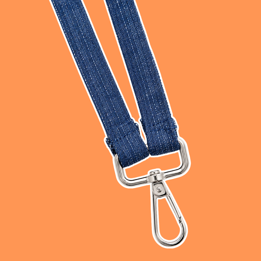 A close-up of a dark blue denim strap with silver metal swivel clasp hardware, set against a solid orange background.