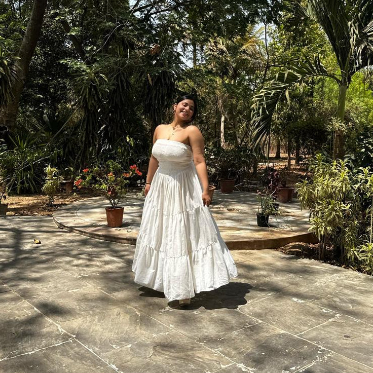 Woman in a white dress standing in a garden with trees and plants around.