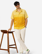 Man wearing a yellow shirt and white pants standing next to a wooden stool on a white background