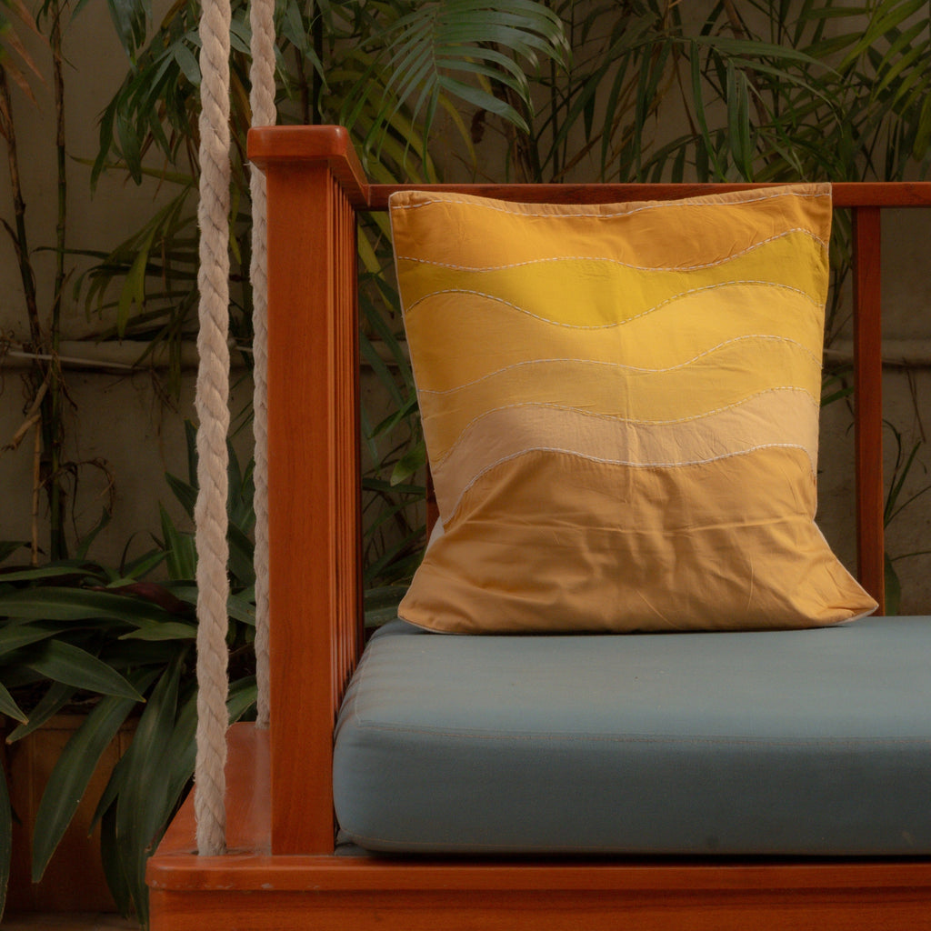 Wooden swing with a yellow cushion and green plants in the background