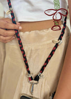 Person wearing a braided black and red phone lanyard with a white top and beige pants.
