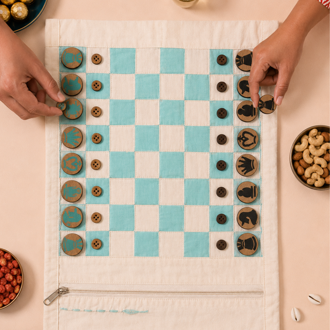 A fabric chess set laid out on a light beige table, featuring a cream and turquoise checkered board, wooden chess pieces, and two hands adjusting the pieces. Surrounding the board are bowls of nuts, red beans, and chocolate-covered chocolates, with a zipper pocket at the bottom of the cloth board.