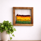 Framed woven wall art with a plant on a wooden surface