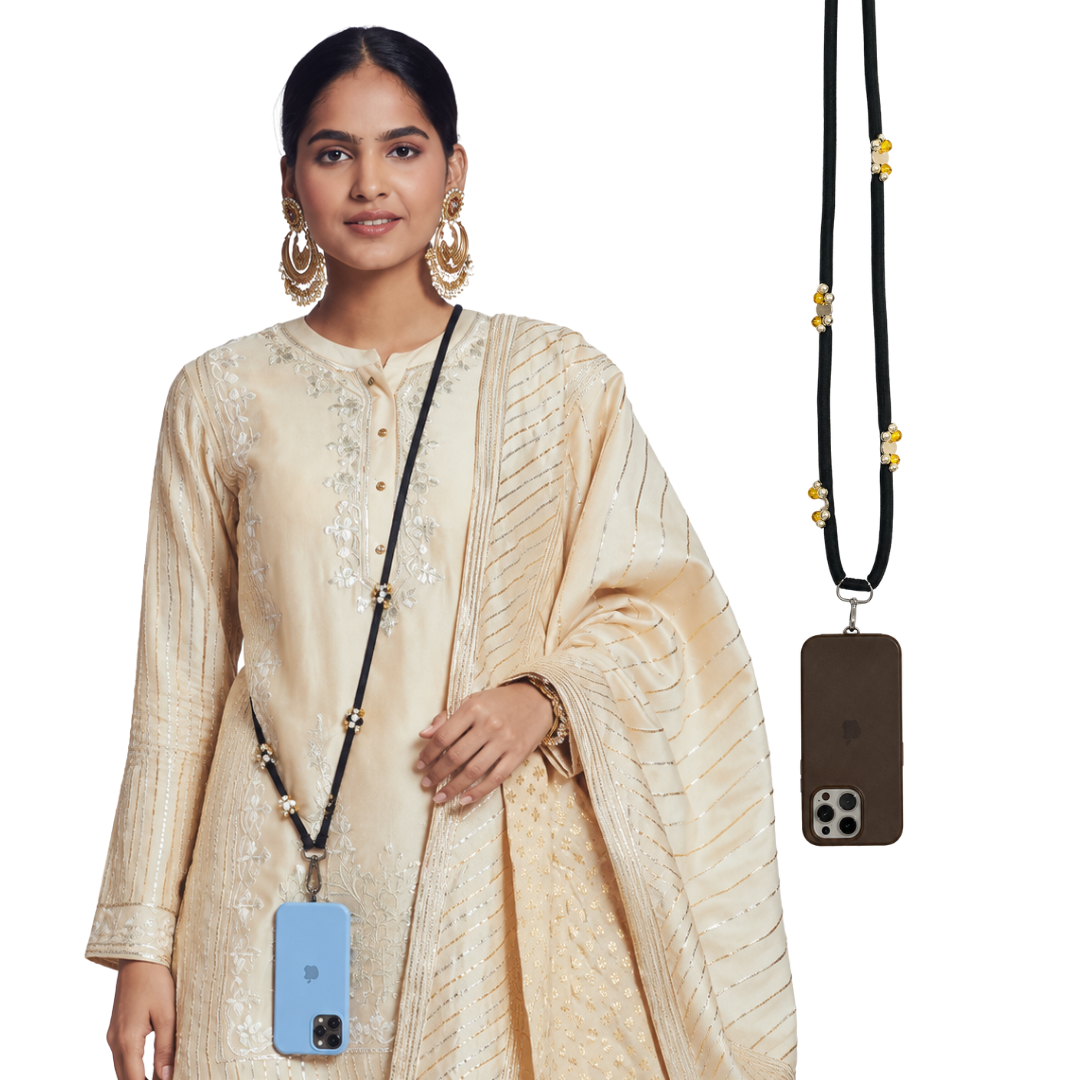 A woman wearing a cream-colored embroidered traditional outfit models a black phone strap with gold bead accents. The phone strap is shown both worn around her neck and hanging on the right side, holding a brown and a light blue smartphone.