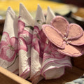 A close-up of folded white napkins with pink floral prints and a matching pink fabric flower embellishment, arranged in a wooden tray.