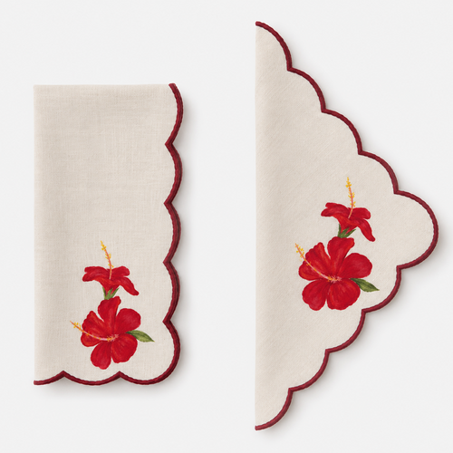 A set of two cream-colored linen napkins with scalloped edges, featuring painted red hibiscus flowers and green leaves, displayed on a light gray background.