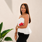 Woman wearing a white top with red floral details and black pants against a beige background