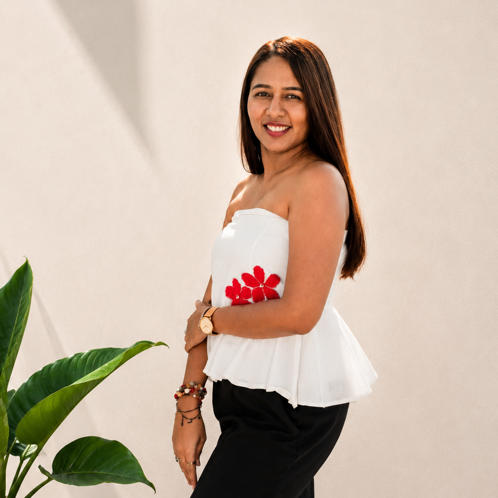 Woman wearing a white top with red floral details and black pants against a beige background