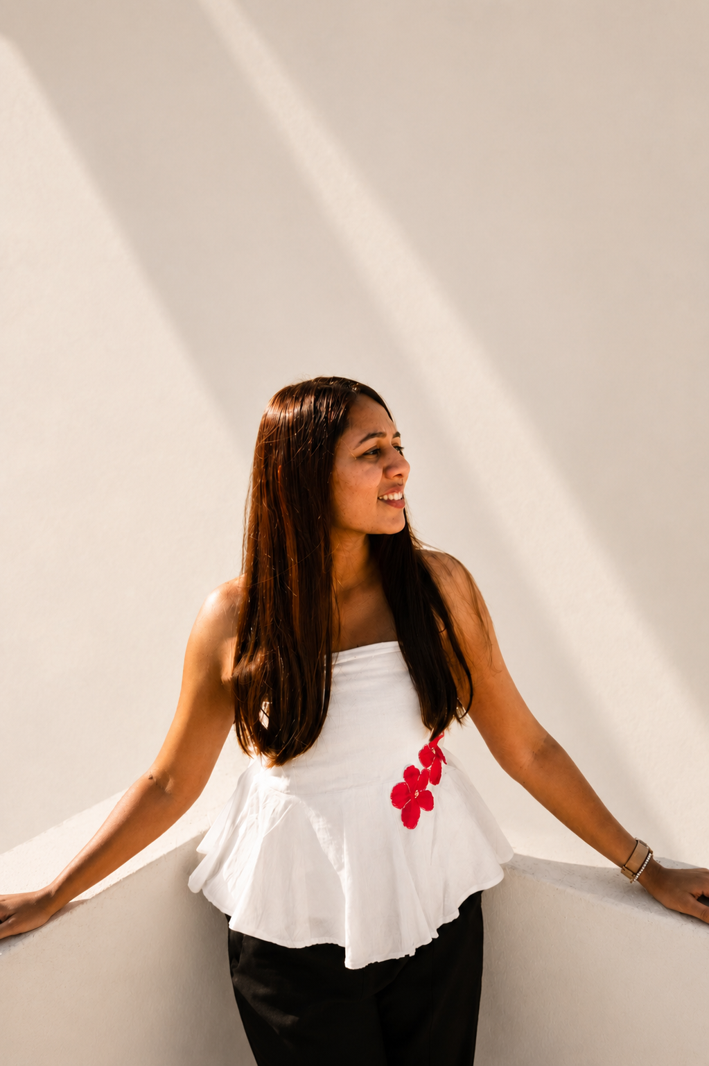 Woman wearing a white top with red floral details against a plain background