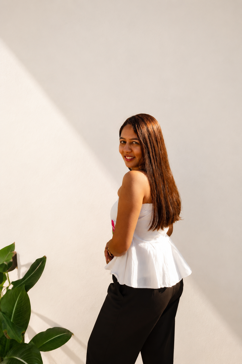 Woman wearing a white top and black pants standing against a light background