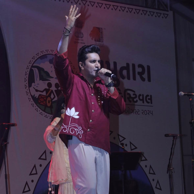 Person on stage with microphone, waving, wearing hand crafted jacket