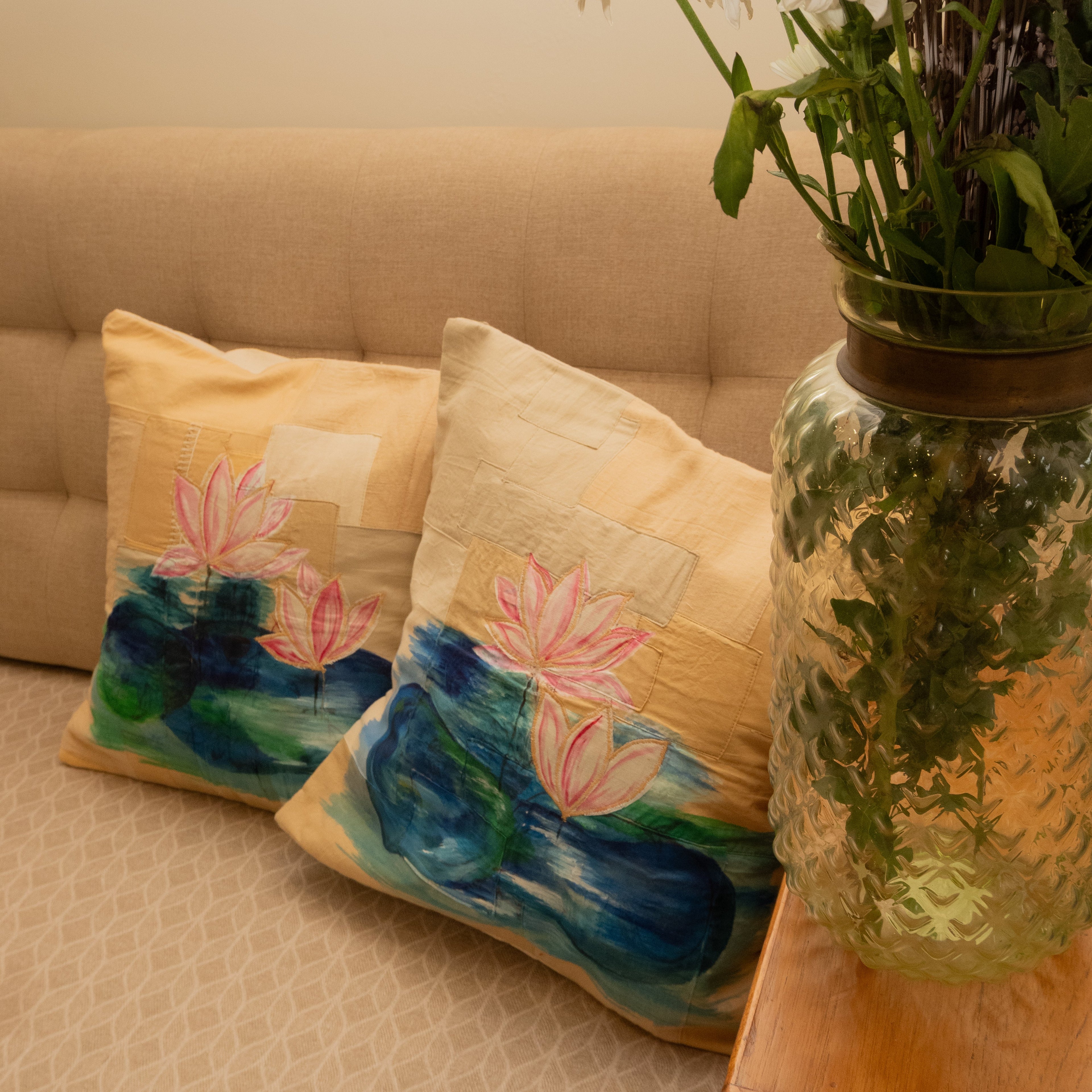 Decorative pillows with floral designs on a beige sofa next to a vase of white flowers.