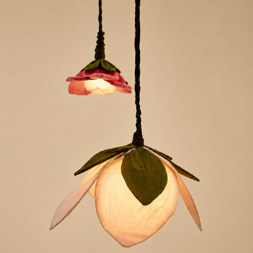 Two hanging flower-shaped pendant lights with black cords, one unlit and one glowing warm white, set against a plain beige background.