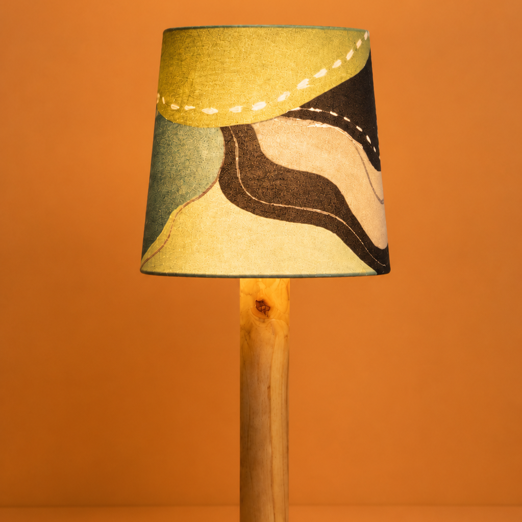A table lamp with a cylindrical patterned fabric shade, a natural wood stem, and a round wooden base, set against a solid orange background.