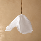 A white fabric flower-shaped pendant light hanging from a twisted brown rope against a warm beige textured background.
