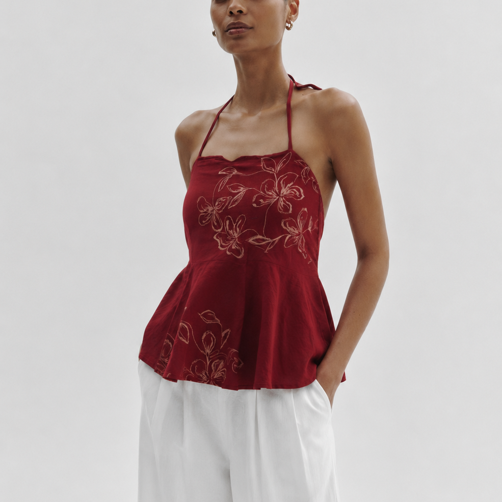 Woman wearing a red floral top and white pants on a plain background