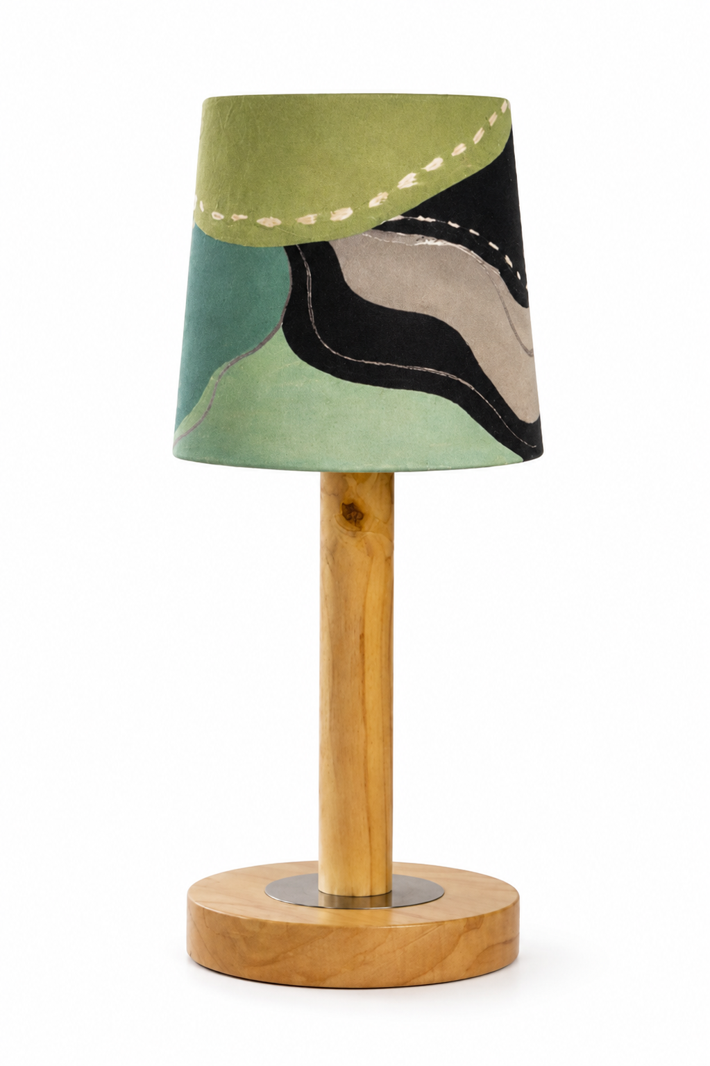 A modern table lamp with a tapered fabric shade featuring an abstract patchwork pattern in sage green, teal, black, and beige, supported by a light natural wood stem and circular wooden base.