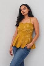 Woman wearing a mustard yellow top with floral patterns and blue jeans against a light gray background