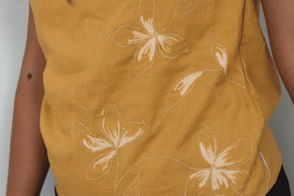 Mustard sleeveless top with white floral patterns on a plain background