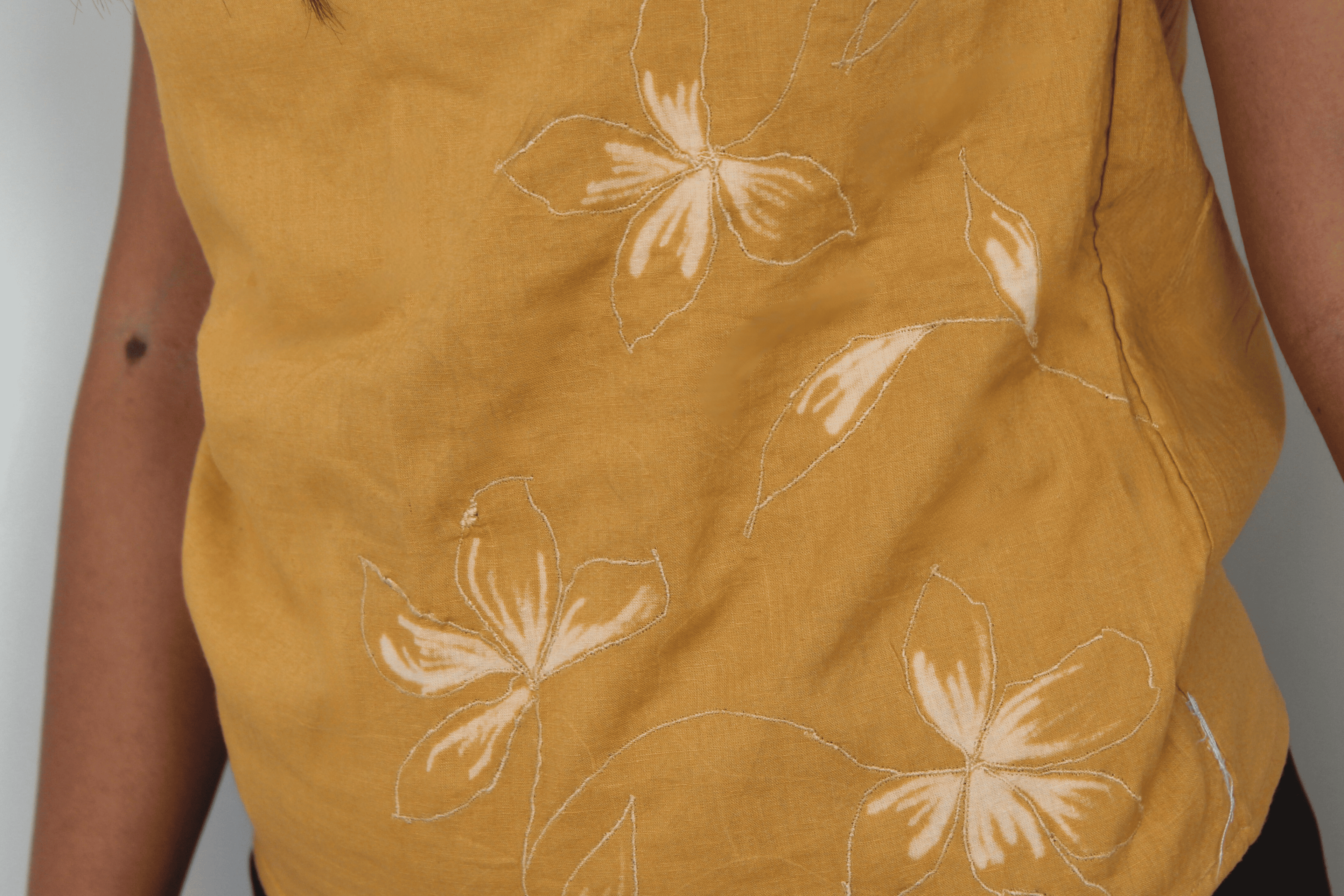 Mustard sleeveless top with white floral patterns on a plain background
