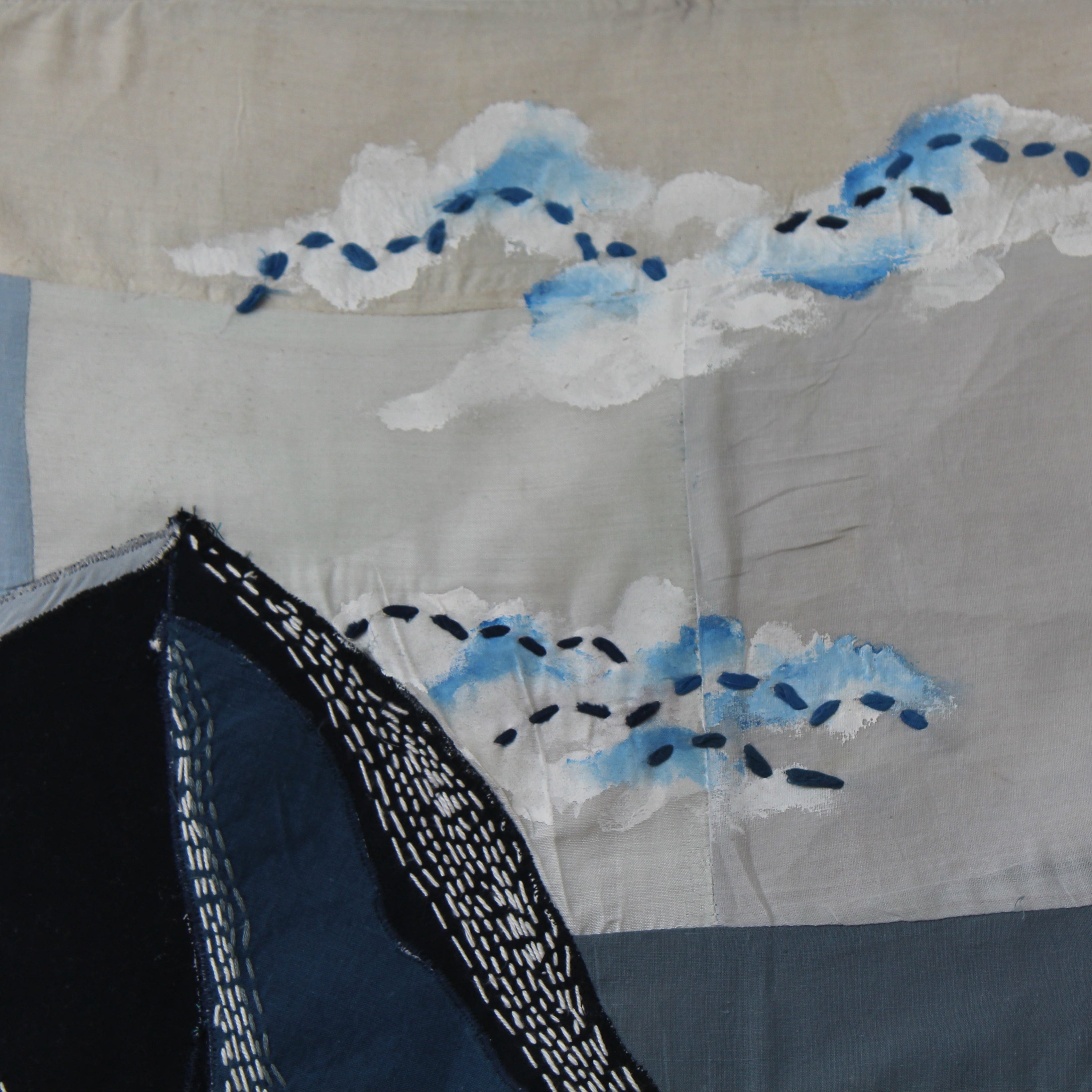 Handmade textile wall art featuring mountain landscape and clouds in deep blue tones, decorative wall art for living rooms, studios and modern interiors.