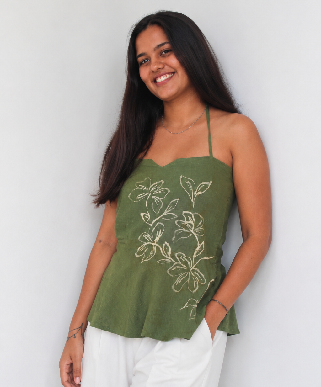 Woman wearing a green floral top and white pants against a light background