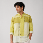 A man wearing a green and cream color-blocked kurta with embroidered details, paired with cream trousers, photographed against a neutral light gray background.