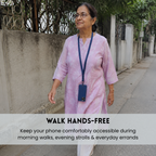 A woman walking outdoors on a sidewalk wearing a light pink patterned kurta and a navy blue lanyard with a phone holder. A text banner at the bottom reads 'WALK HANDS-FREE' with additional descriptive text.