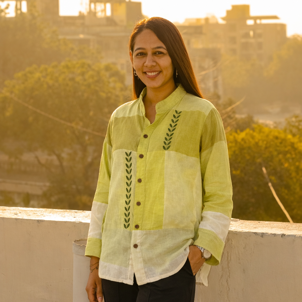 Woman wearing a light green and white patterned shirt on a rooftop with a cityscape in the background.
