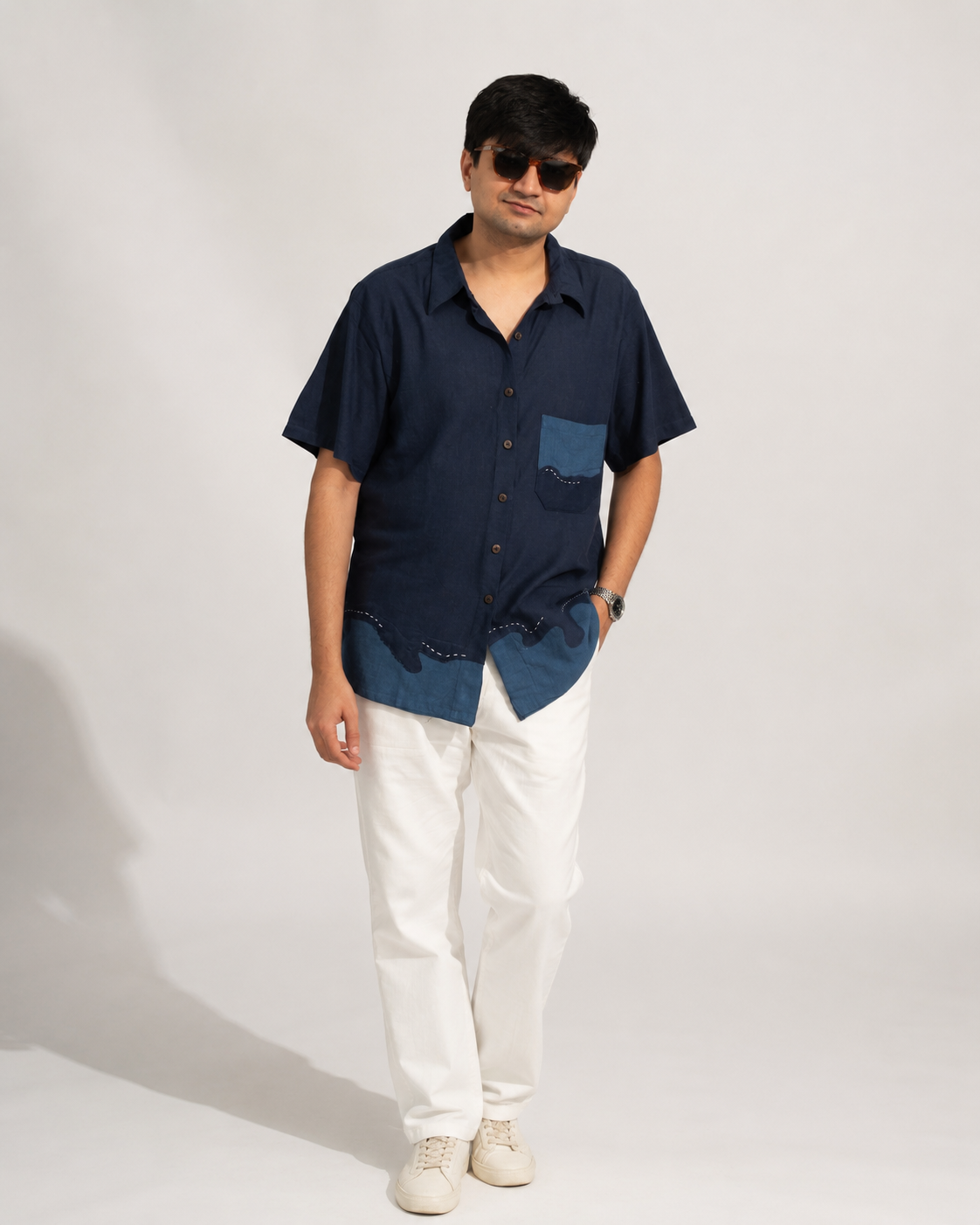 Man wearing a navy shirt with a denim patch and white pants on a plain background