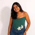 Woman wearing a green strapless corset top with floral designs and blue jeans on a white background