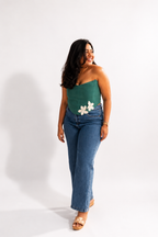 Woman wearing a green strapless top with floral designs and blue jeans on a white background