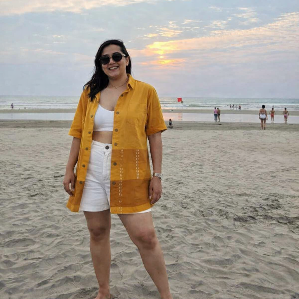 Woman in yellow shirt and white shorts standing on a beach with a sunset in the background