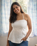 Woman wearing a white top and blue jeans standing in a room with light curtains.