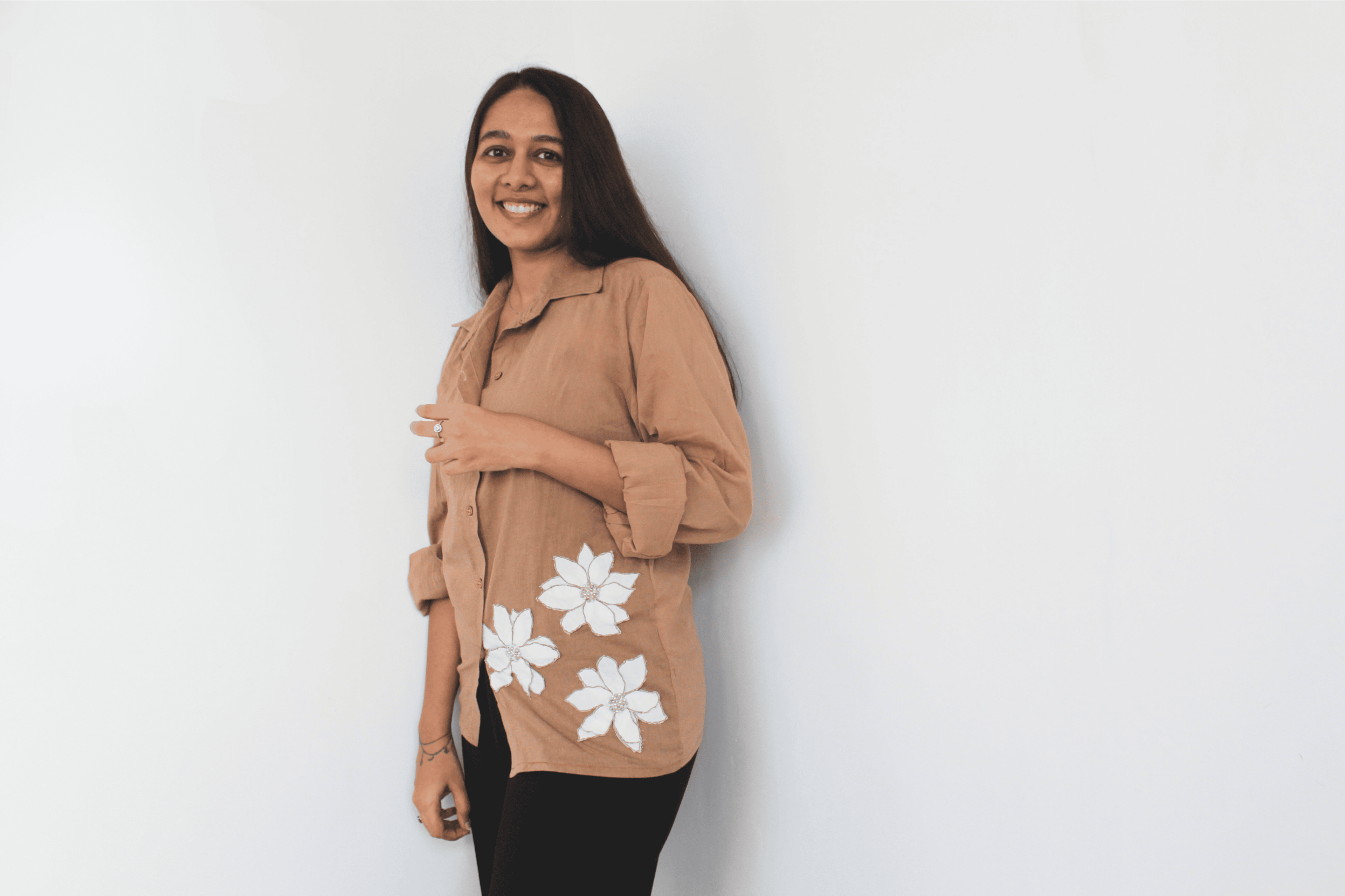 Woman wearing a beige shirt with white floral patterns on a plain background