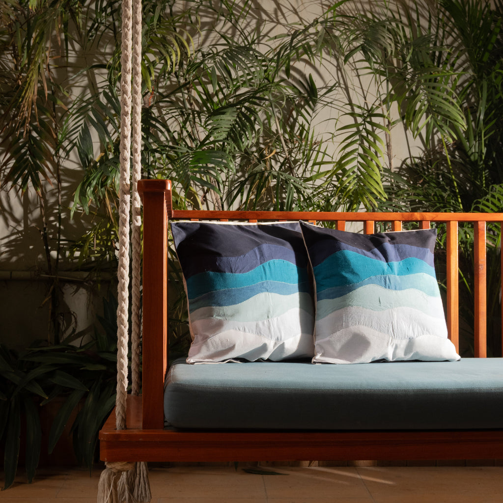 Wooden swing with blue and white striped cushions against a wall with plants