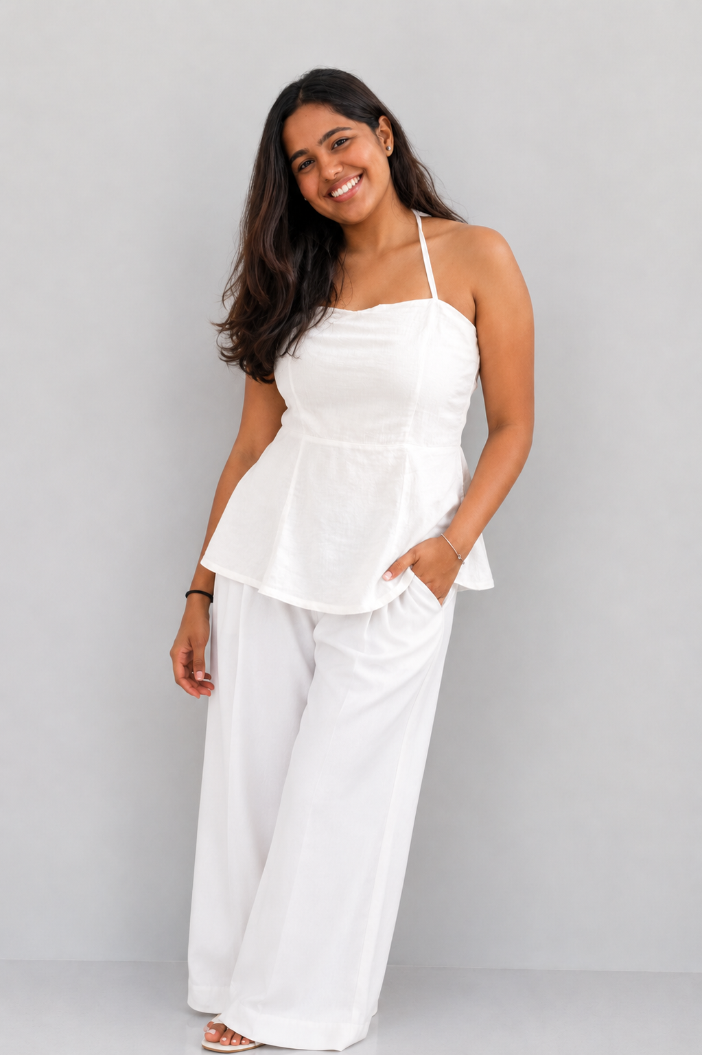 Woman wearing a white peplum top and wide-leg pants against a gray background