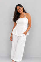 Woman wearing a white peplum top and wide-leg pants against a gray background