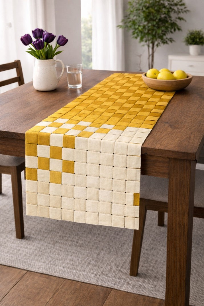 Yellow and white woven table runner on a wooden table with a vase of purple tulips and a bowl of lemons.