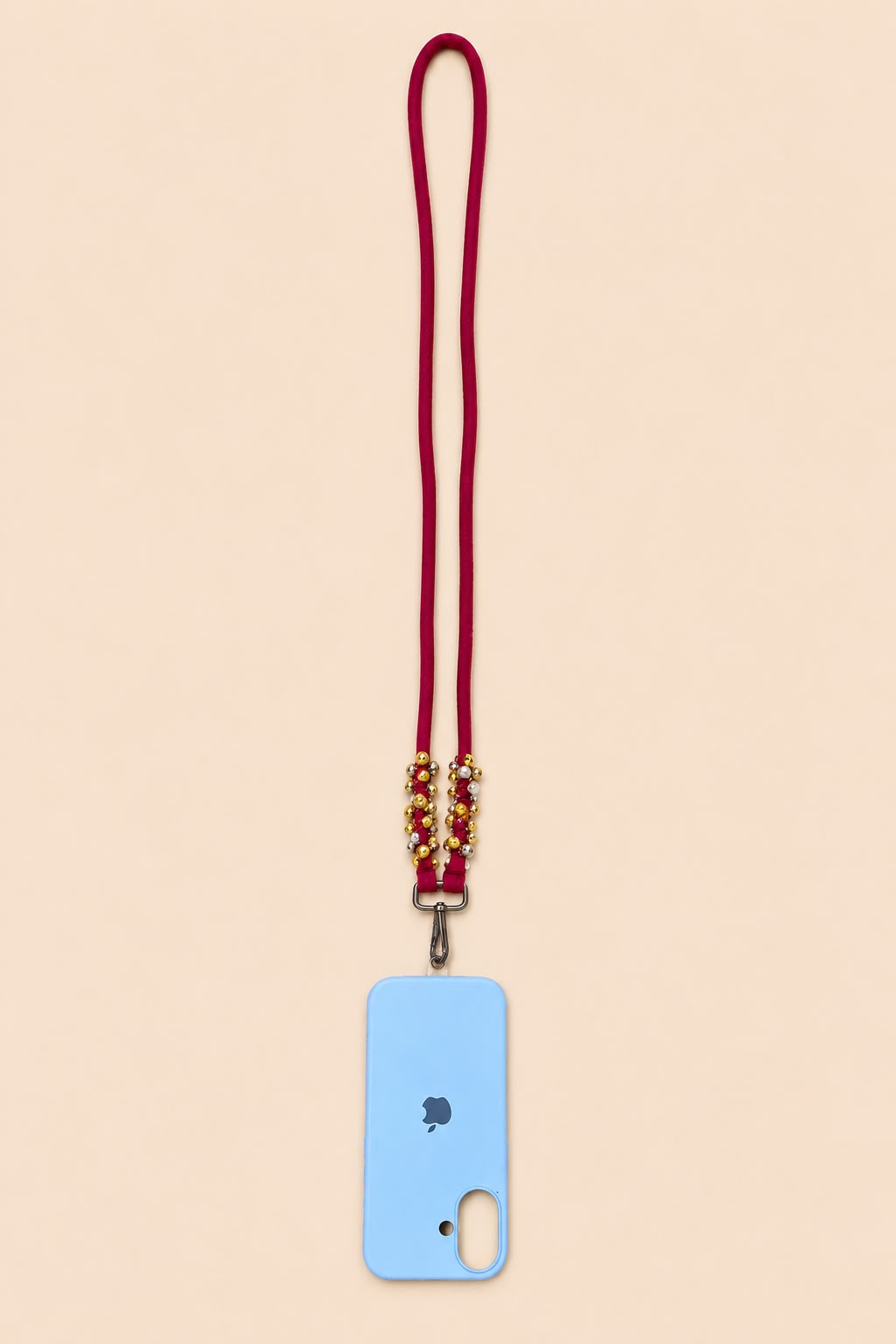 A light blue phone case with a matching red cord lanyard and gold-toned decorative beads, shown on a solid pale peach background.